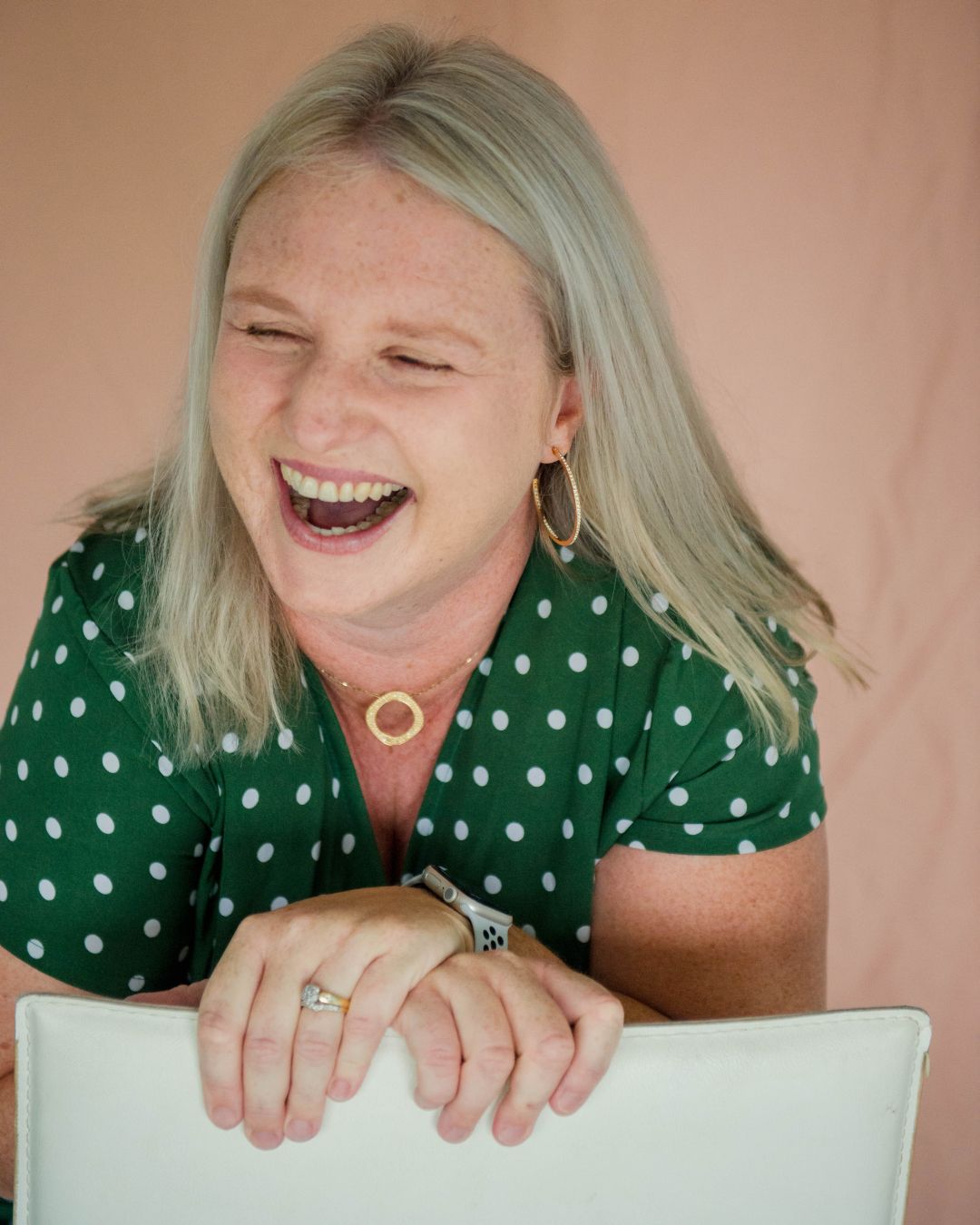 Perimenopausal woman in a green polka dot shirt laughing with a pink background.  woman with radiant skin using ReCellience UCX exosome moisturiser